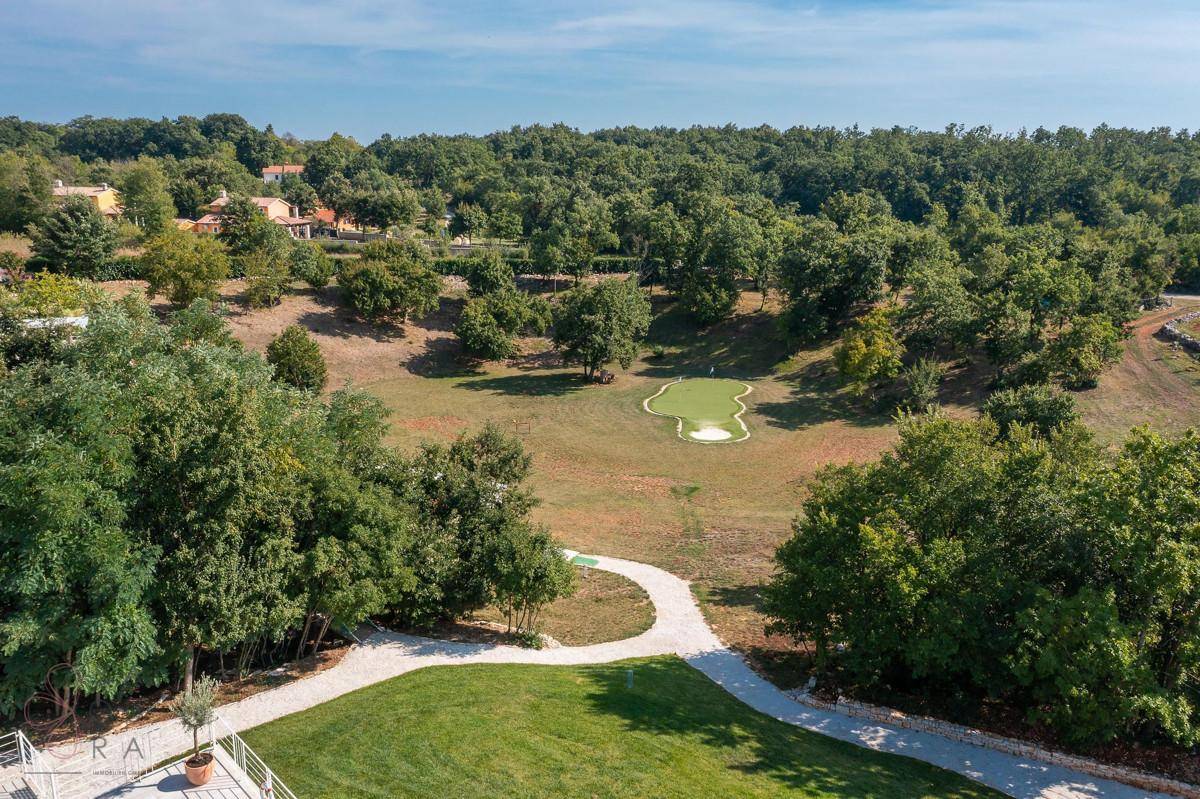 Weitläufige grüne Landschaft mit einem Golf-Putting-Green, umgeben von Bäumen und einem Spazierweg.