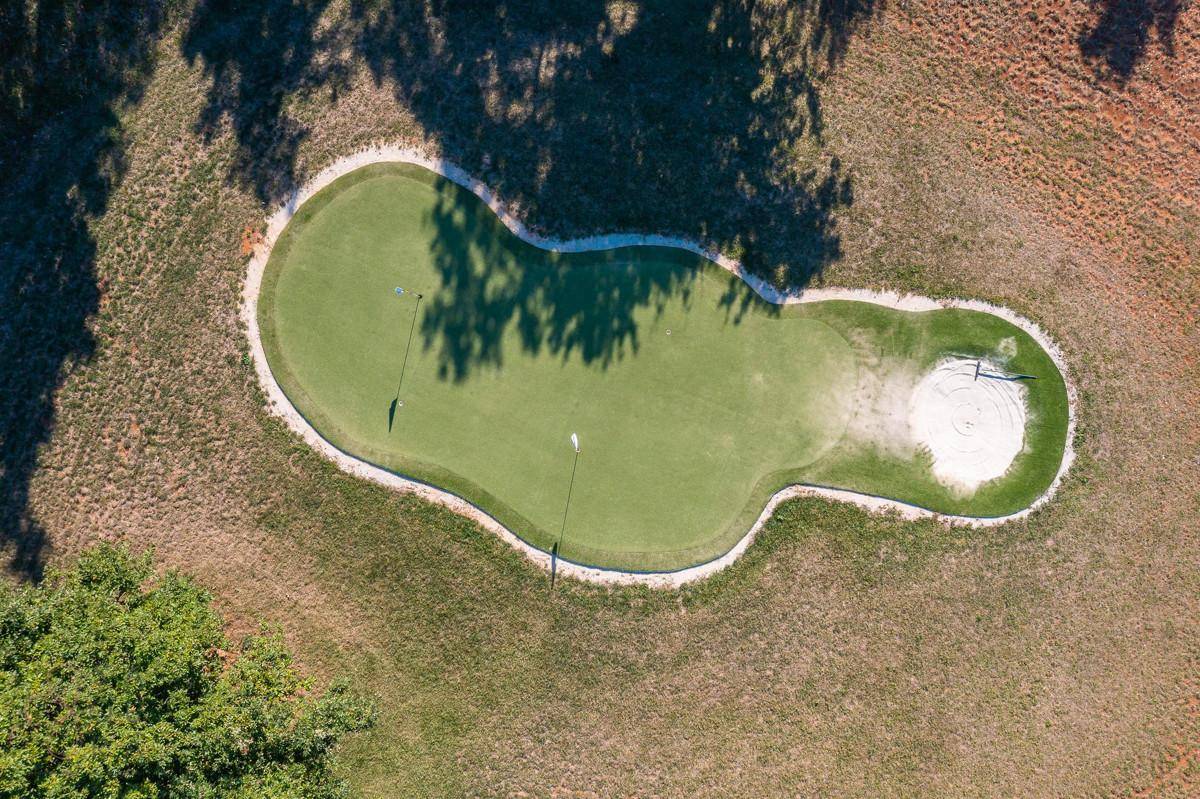 Luftaufnahme eines detaillierten Golf-Putting-Greens mit zwei Fahnen und einem Sandbunker.