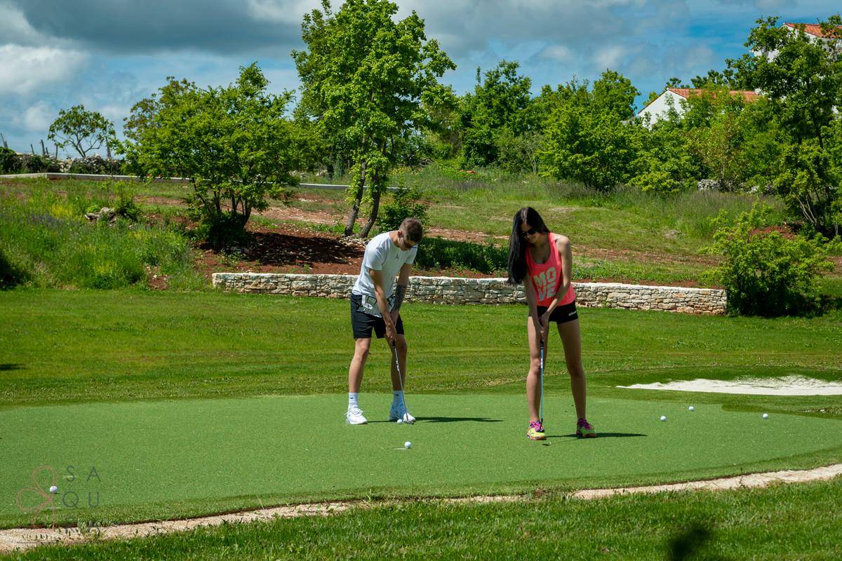 Zwei Personen beim Putten auf dem Golf-Green, umgeben von üppiger grüner Vegetation und Bäumen.
