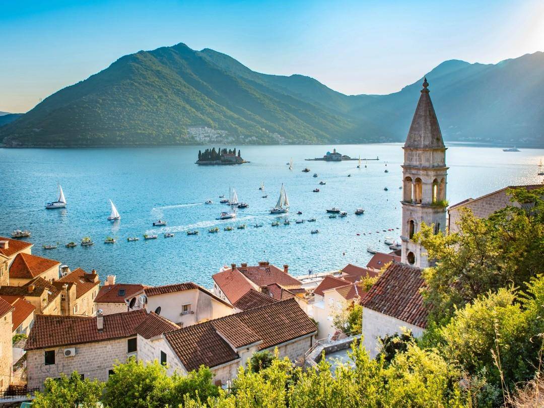 Malerische Küstenstadt mit historischen Gebäuden, Bergen und Segelbooten im Meer bei Sonnenschein.