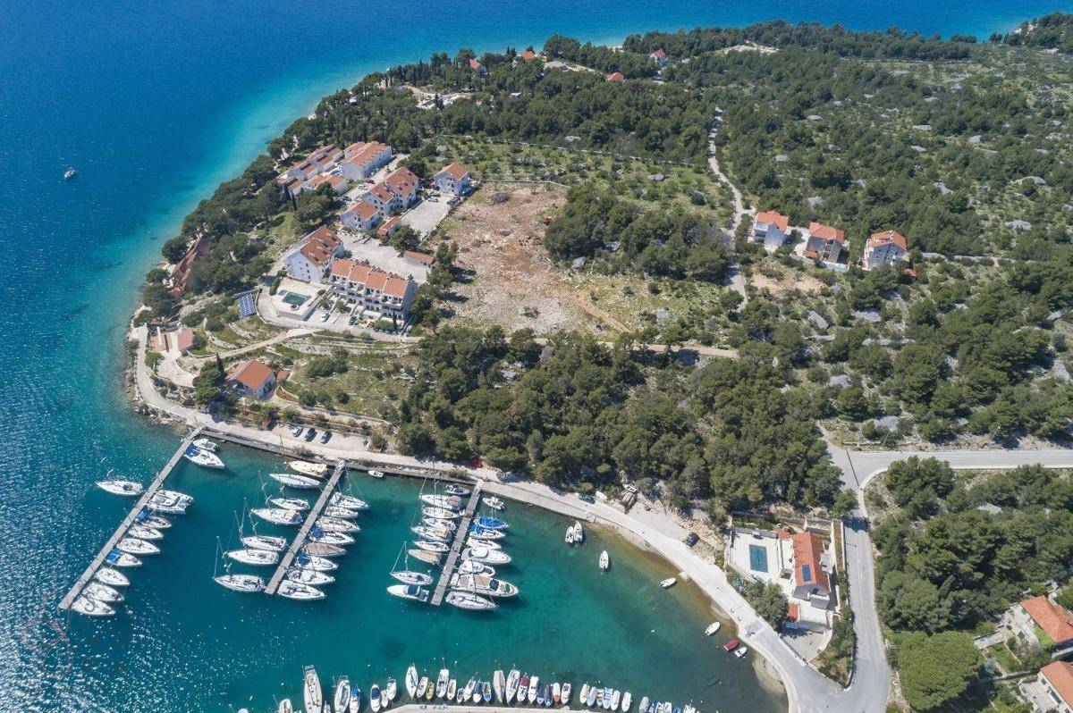 Vogelperspektive auf eine Bucht mit Yachthafen, mehreren Gebäuden und einem Swimmingpool in grüner Umgebung.
