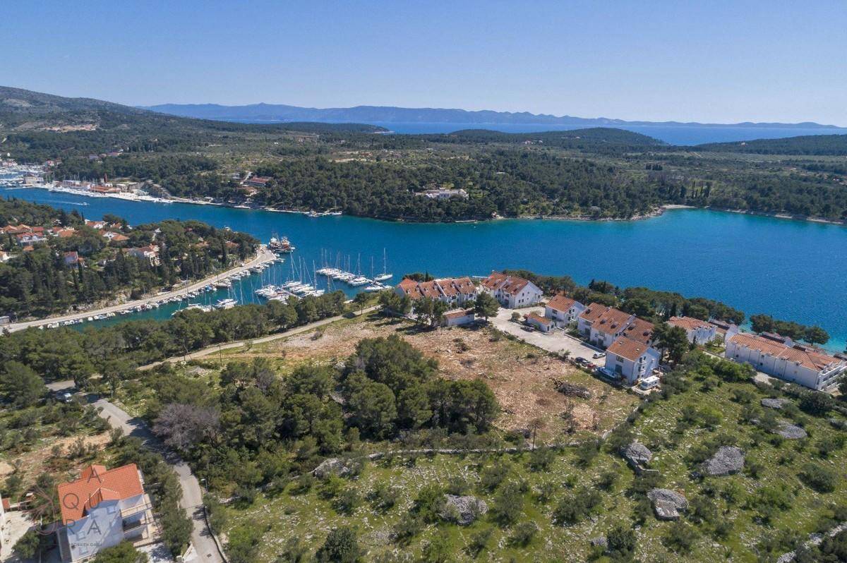 Panoramablick aus der Luft auf eine Bucht mit Yachthafen, mehreren Gebäuden und einem großen unbebauten Grundstück.
