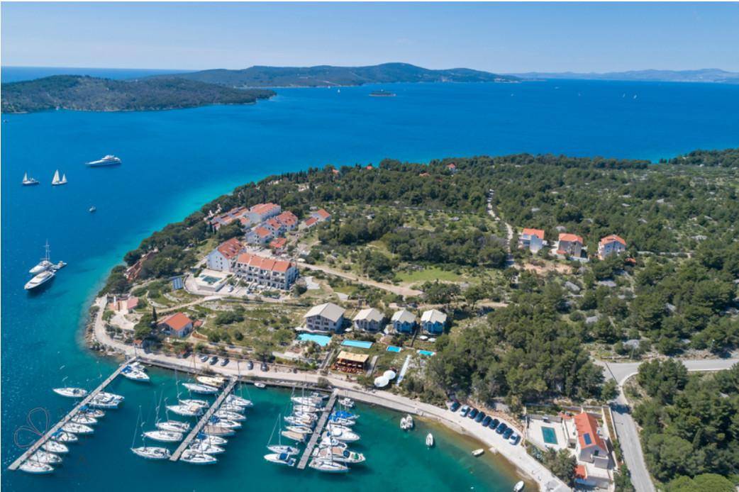 Panoramablick aus der Luft auf eine Küstenanlage mit Yachthafen, Hotels und einem Poolbereich am Meer.