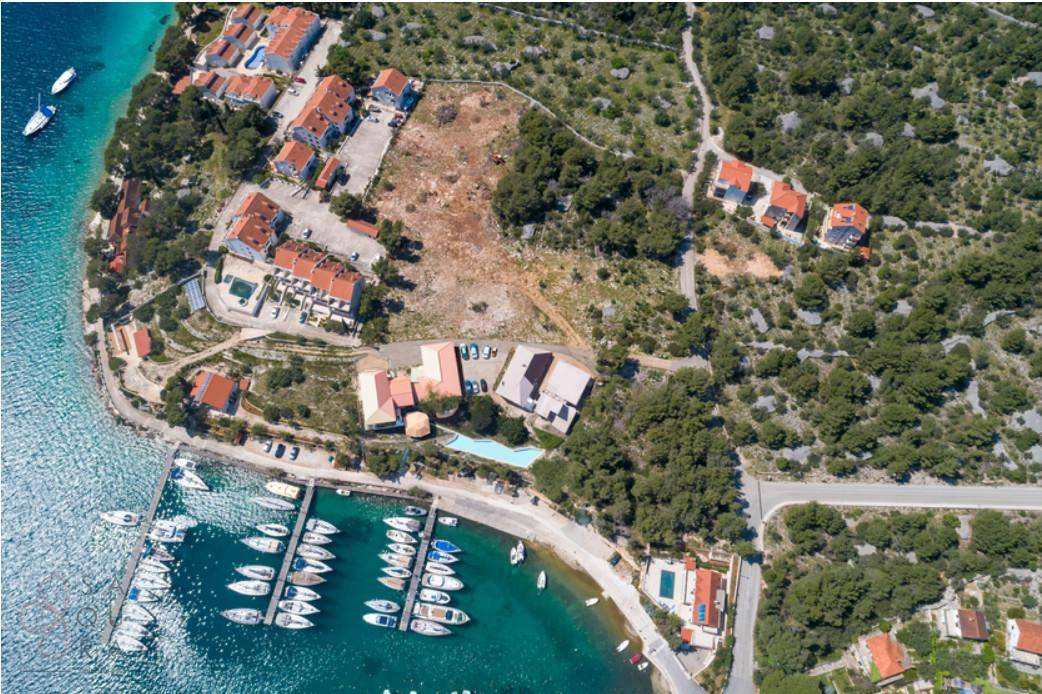 Senkrechte Luftaufnahme eines Yachthafens mit angrenzenden Gebäuden, einem Pool und einem großen unbebauten Grundstück.