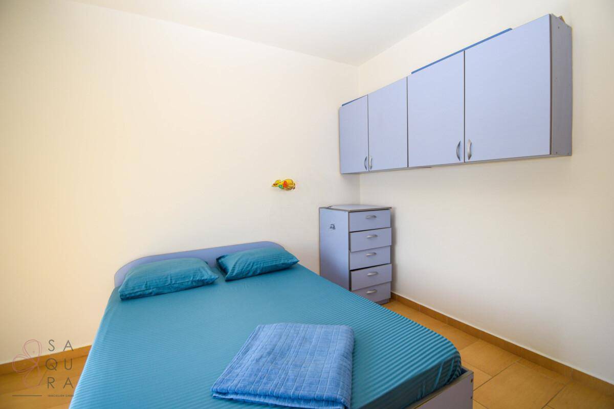 Helles Schlafzimmer mit Einzelbett, Hängeschränken und einer Kommode.