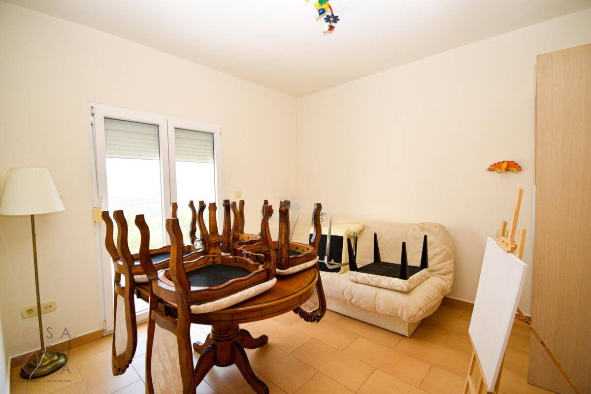 Esszimmer mit Holztisch und Stühlen, ergänzt durch eine kleine Couch und eine Staffelei.