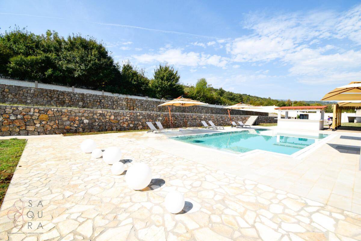 Heller Poolbereich mit dekorativen Kugeln, Sonnenliegen und Sonnenschirmen auf Steinplatten.