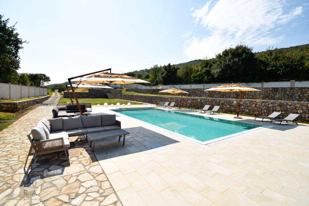 Geräumiger Poolbereich mit bequemer Outdoor-Sitzgruppe, Sonnenliegen und Sonnenschirmen.