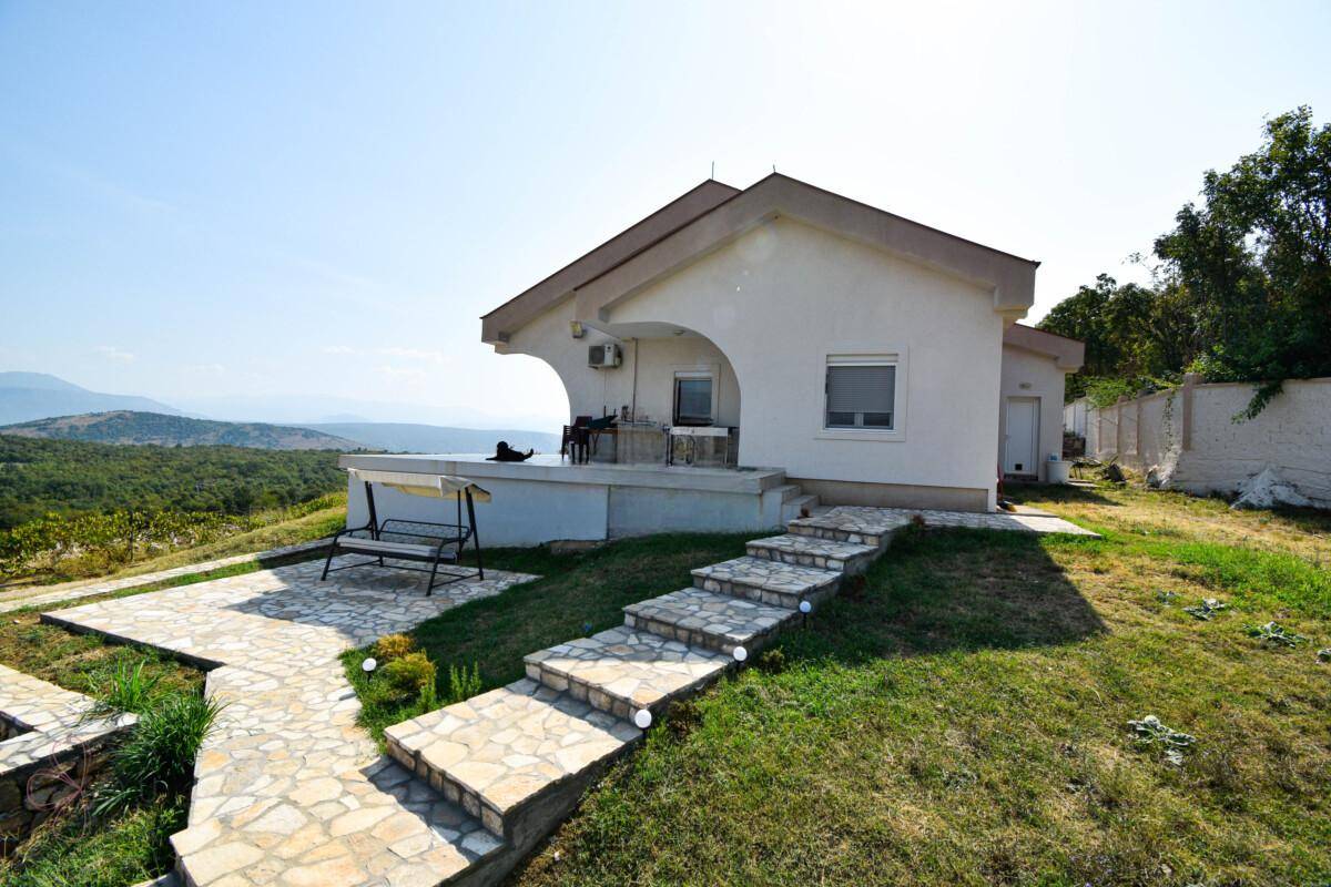 Hausansicht mit Steintreppe, gepflasterter Terrasse und Schaukelbank, mit weitem Blick in die Landschaft.