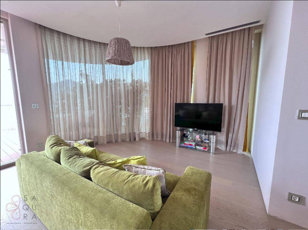 Gemütliches Wohnzimmer mit grüner Couch und großen, geschwungenen Fenstern, die viel Licht hereinlassen.