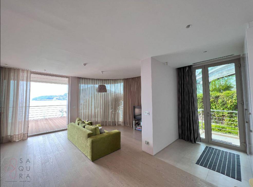 Geräumiger Wohnbereich mit Holzboden und großen Fenstern, die Zugang zu einem Balkon bieten.
