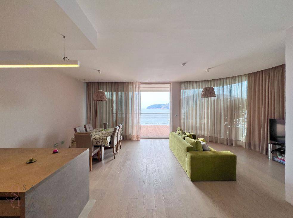 Heller Wohn- und Essbereich mit Holzboden, grüner Couch und Zugang zu einem Balkon mit Meerblick.