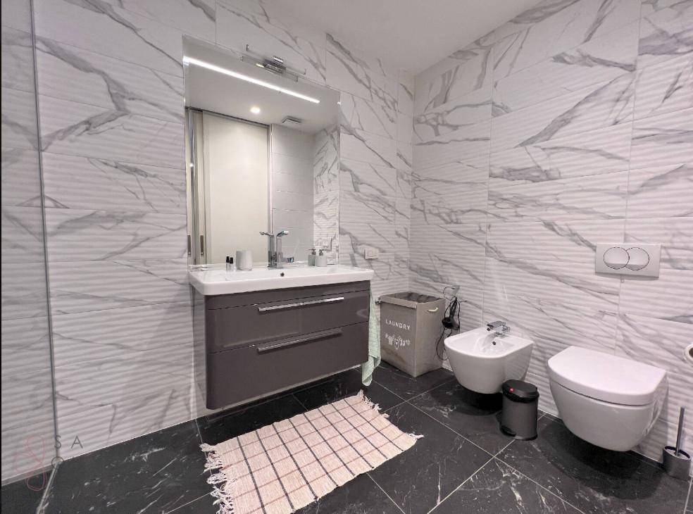 Elegantes Badezimmer mit Marmorfliesen, Bidet, wandhängendem WC und modernem Waschtisch.