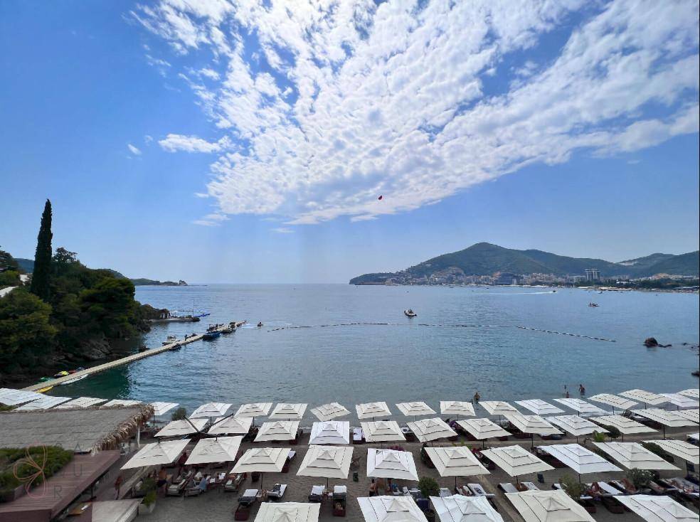 Panoramablick auf das Meer mit Strand, Sonnenschirmen und umliegenden Bergen.