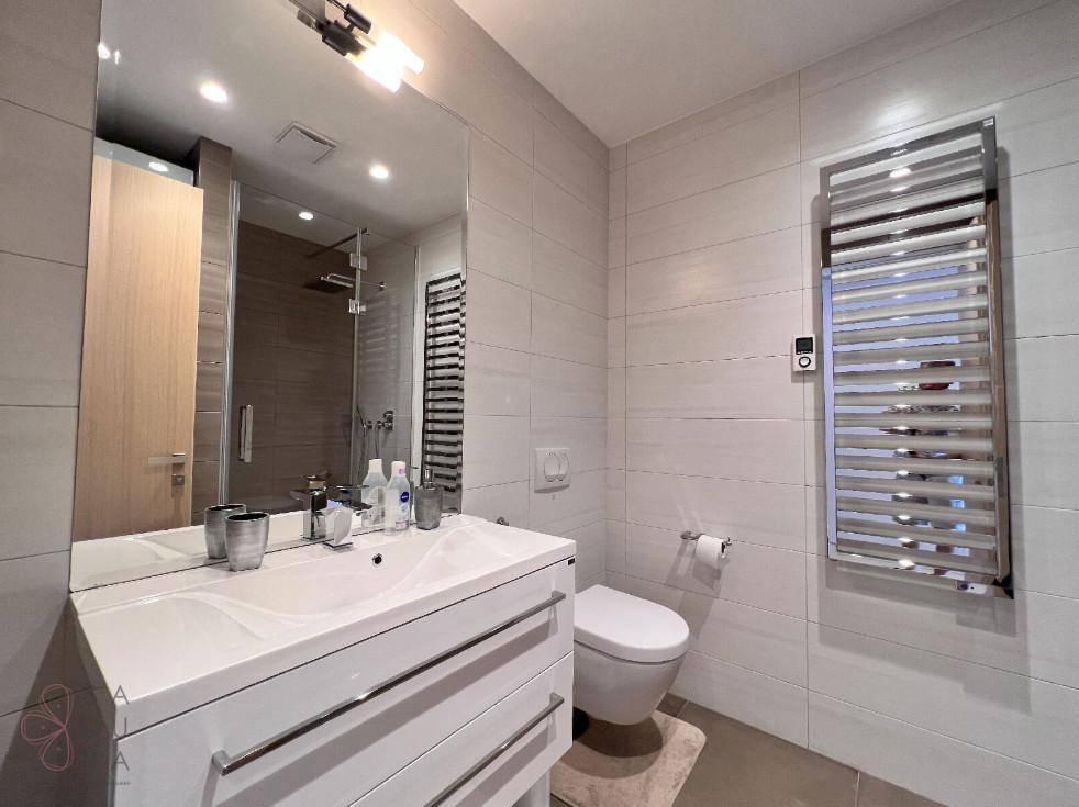 Helles Badezimmer mit modernem Waschtisch, WC, Dusche und beheiztem Handtuchhalter.