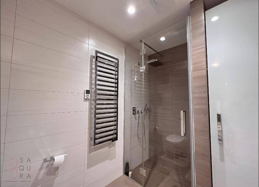 Modernes Badezimmer mit begehbarer Dusche, beheiztem Handtuchhalter und hellen Fliesen.