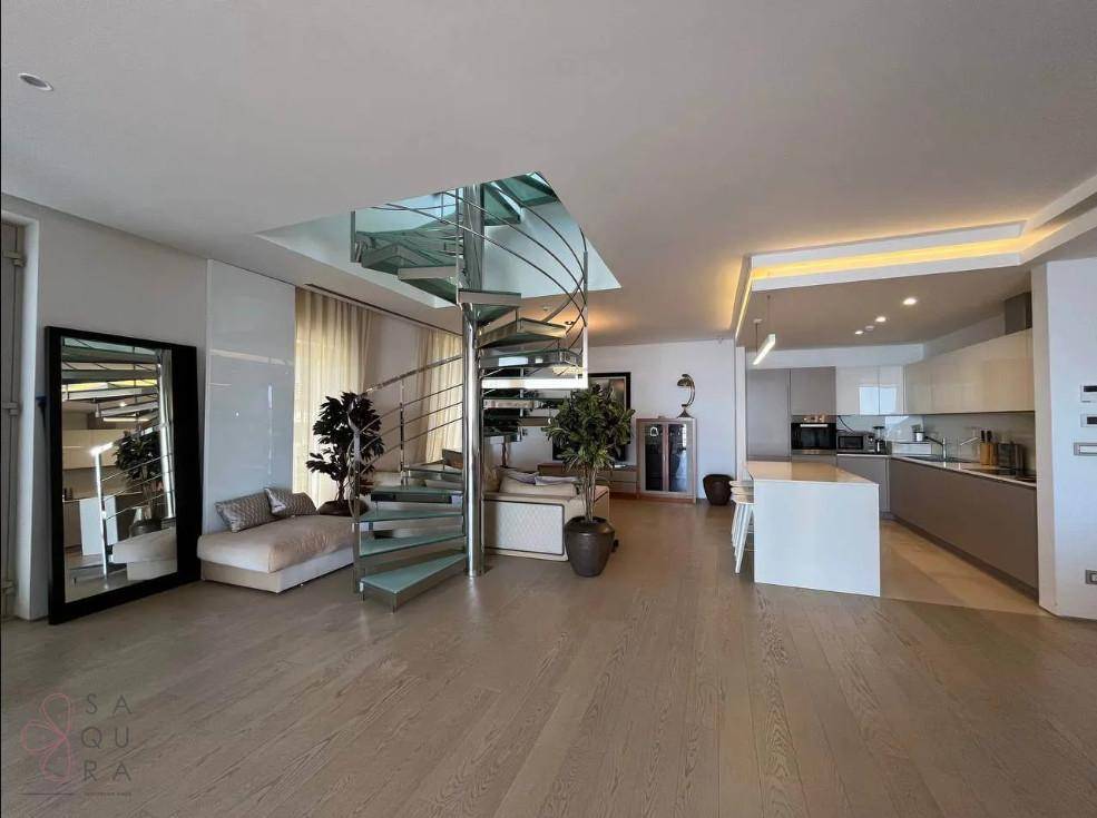 Offener Wohnbereich mit eleganter Wendeltreppe, Holzboden und integrierter moderner Küche im Hintergrund.