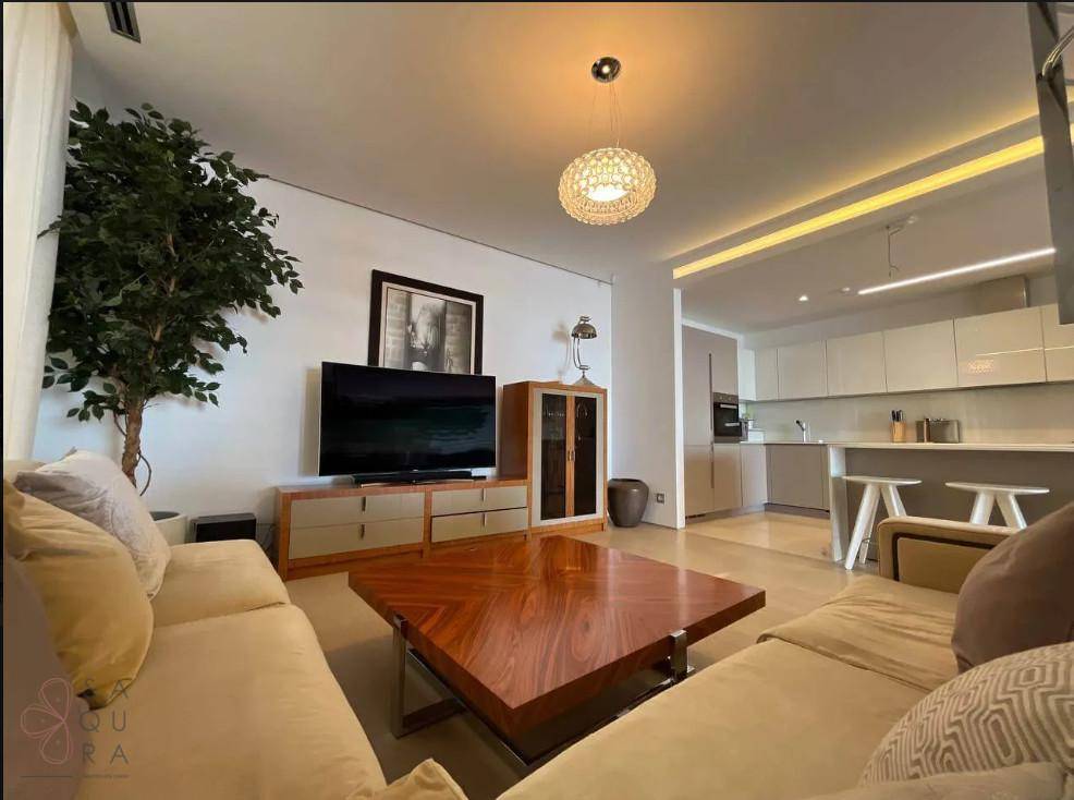 Gemütliches Wohnzimmer mit beigem Sofa, Holztisch und offener Verbindung zur Küche.