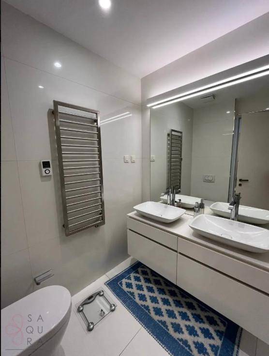 Modernes Badezimmer mit Doppelwaschbecken, beheiztem Handtuchhalter und weißen Fliesen.