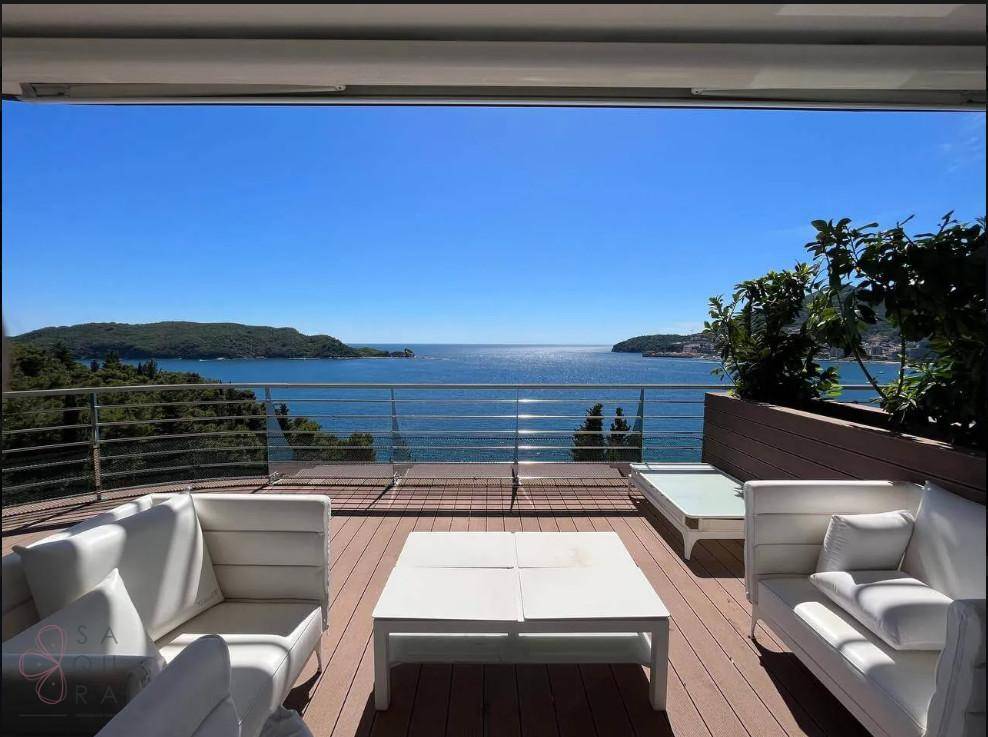 Helle Terrasse mit weißen Lounge-Möbeln und unverbautem Blick auf das weite Meer.