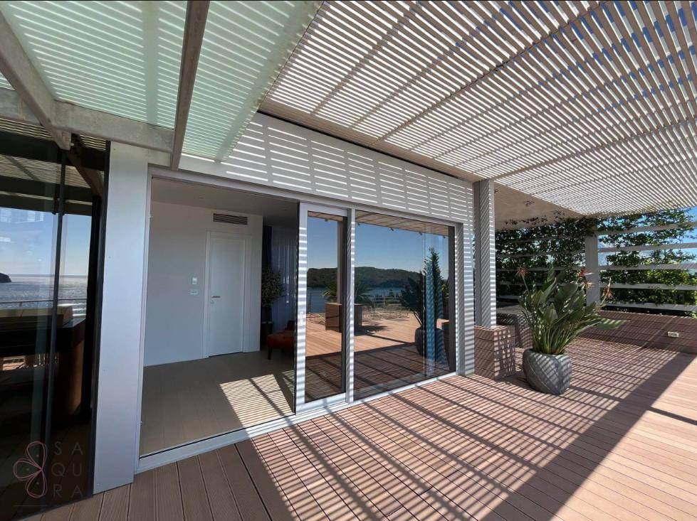 Terrasse mit großen Glasschiebetüren zum Innenbereich und weitem Meerblick unter einer Pergola.