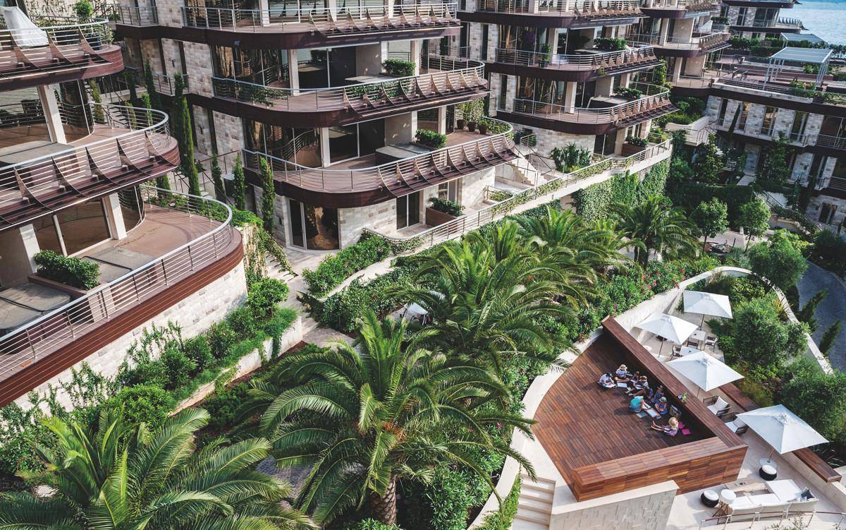 Luftaufnahme eines luxuriösen Wohnkomplexes mit Terrassen, üppigen Gärten und Meerblick.