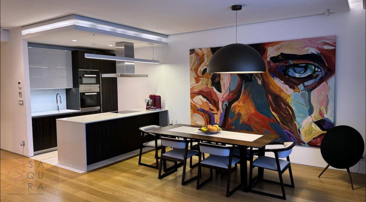Stilvoller Essbereich mit Holztisch und moderner offener Küche mit Kochinsel und integrierten Geräten.