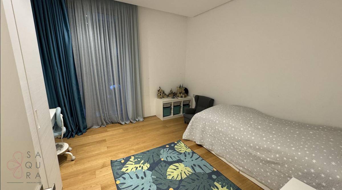 Kinderzimmer mit Einzelbett, farbenfrohem Teppich und blauen Vorhängen, bietet eine gemütliche Atmosphäre.