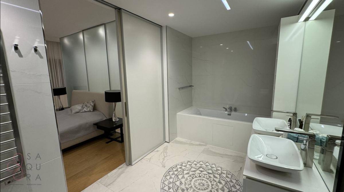 Helles Badezimmer mit Badewanne, modernem Waschbecken und Zugang zum Schlafzimmer.