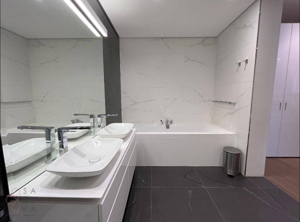Modernes Badezimmer mit Doppelwaschbecken, integrierter Badewanne und eleganten Marmorfliesen an Wänden und Boden.
