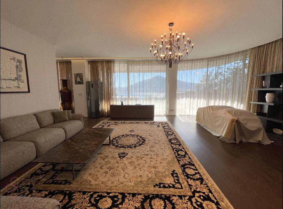 Elegantes Wohnzimmer mit Panoramablick auf Berge und Wasser durch große, geschwungene Fensterfronten.
