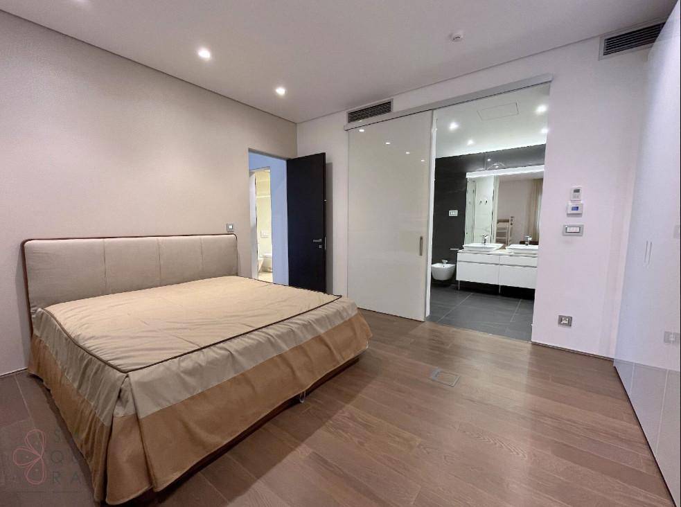 Modernes Schlafzimmer mit Doppelbett und direktem Zugang zu einem luxuriösen Badezimmer durch eine Glasschiebetür.