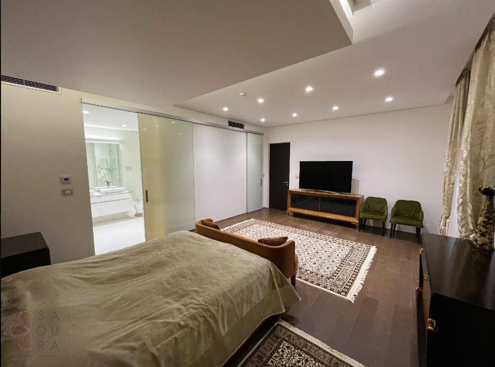 Helles Hauptschlafzimmer mit Bett, Kommode und direktem Zugang zum luxuriösen Badezimmer durch eine Glasschiebetür.