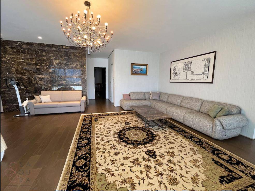 Großzügiges Wohnzimmer mit beigem Ecksofa, opulentem Teppich und dunkler Akzentwand, die Eleganz verleiht.