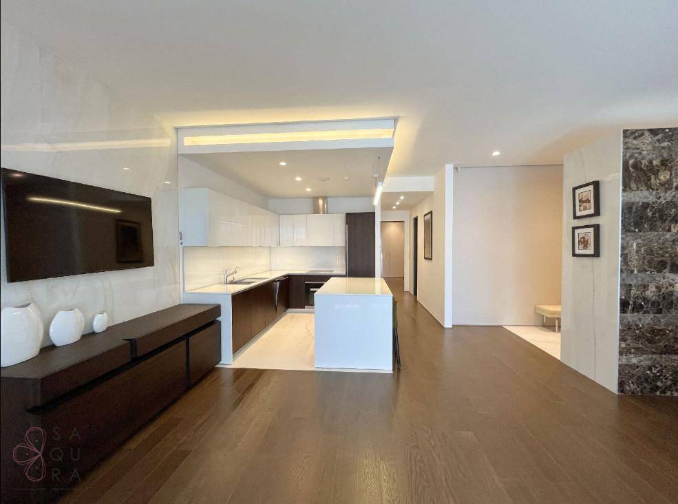 Moderne offene Küche mit Kochinsel, dunklem Holzboden und weißen Hochglanzschränken in einem geräumigen Wohnbereich.