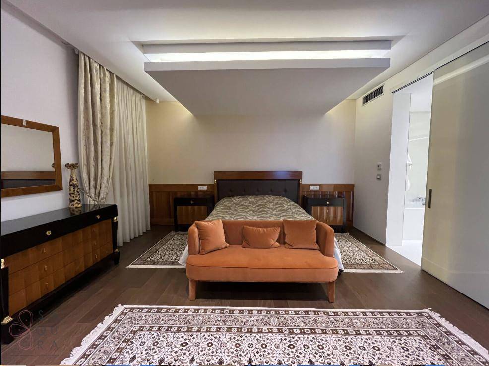 Elegantes Hauptschlafzimmer mit großem Bett, orangefarbenem Sofa, dunklen Holzmöbeln und zwei gemusterten Teppichen.