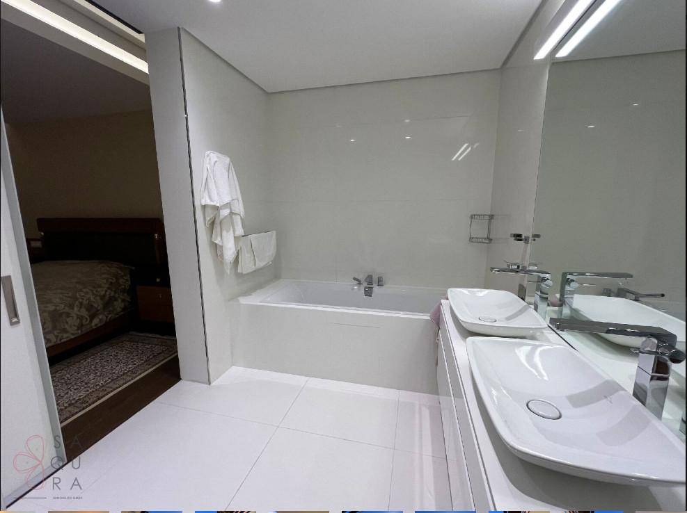 Helles Badezimmer mit Doppelwaschbecken, integrierter Badewanne und weißen Fliesen, mit Blick ins Schlafzimmer.
