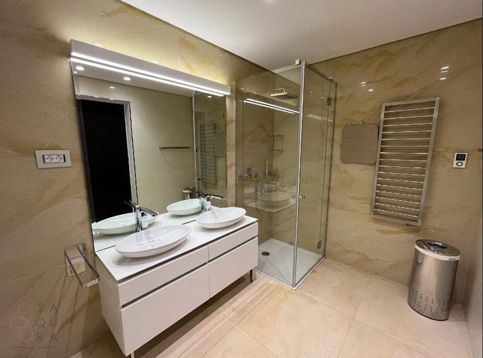 Elegantes Badezimmer mit Doppelwaschbecken, begehbarer Dusche und beigefarbenen Marmorfliesen für ein warmes Ambiente.