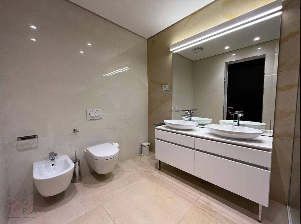 Stilvolles Badezimmer mit Doppelwaschbecken, wandhängendem WC und Bidet, umgeben von beigefarbenen Fliesen.