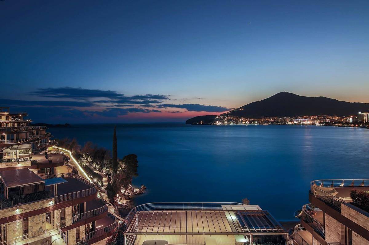 Abendlicher Blick auf die luxuriöse Wohnanlage mit beleuchteten Terrassen und der Stadtkulisse am Meer.
