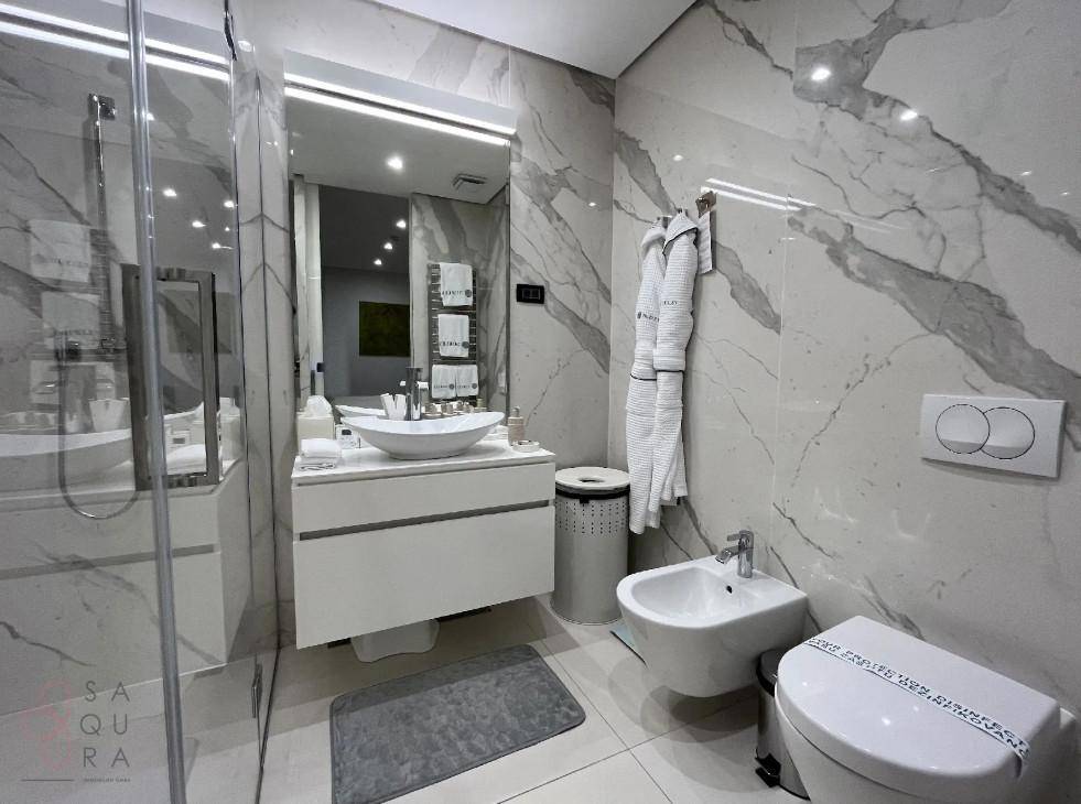 Modernes Badezimmer mit Marmorfliesen, Waschtisch, Bidet und begehbarer Dusche.