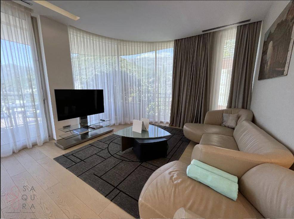 Gemütliches Wohnzimmer mit beigem Ledersofa, Teppich und großen Fenstern, die viel Licht hereinlassen.