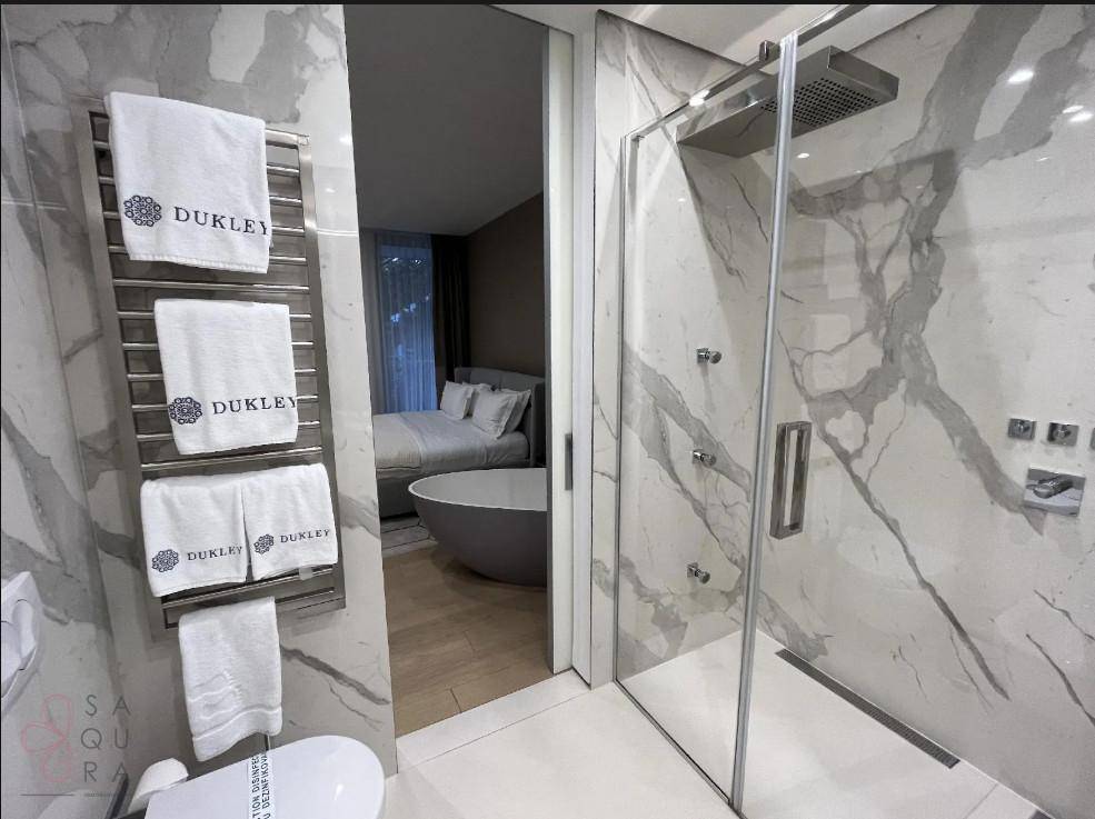 Elegantes Badezimmer mit großer begehbarer Dusche und Blick ins Schlafzimmer mit Badewanne.