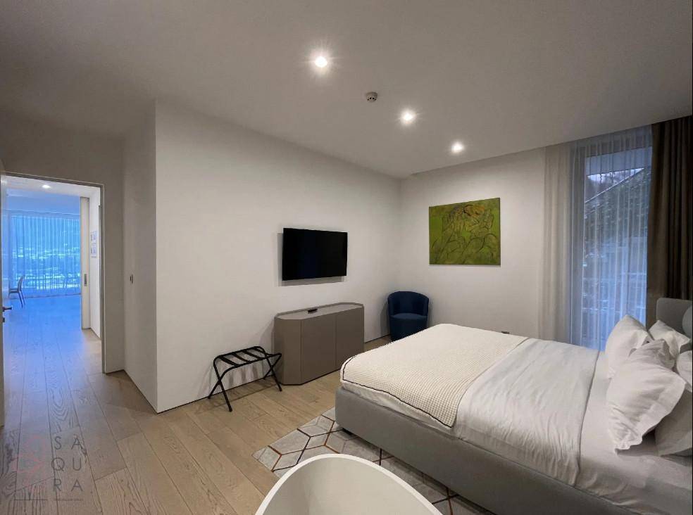 Helles Schlafzimmer mit Fernseher, Holzboden und Zugang zu einem weiteren Wohnbereich.