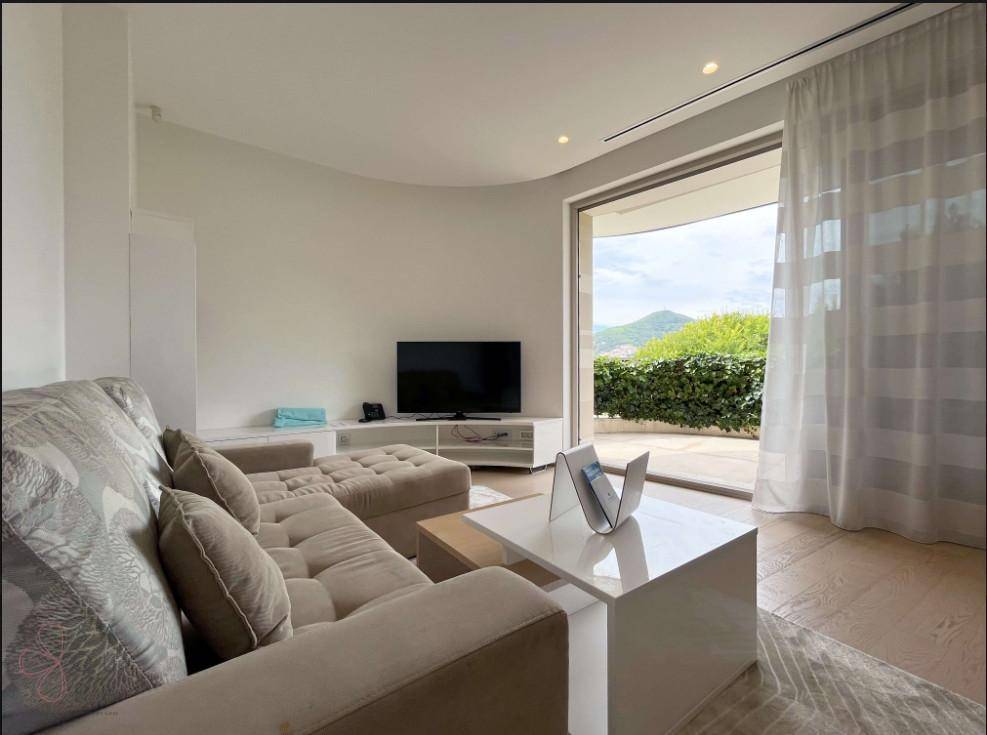 Gemütliches Wohnzimmer mit großem Sofa und Zugang zu einer Terrasse mit grüner Hecke.