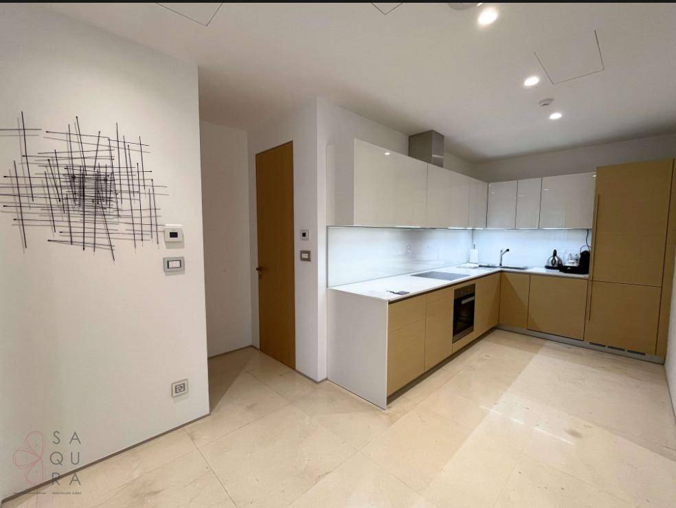 Moderne Küche mit hellen Holz- und weißen Hochglanzschränken, weißen Arbeitsplatten und Fliesenboden.