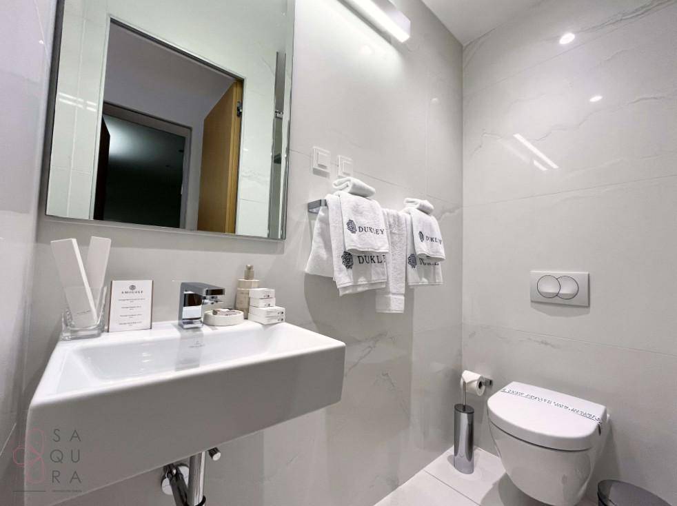 Kleines, modernes Badezimmer mit Wandwaschbecken, Toilette und hellen Marmorfliesen.