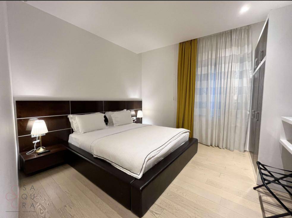 Helles Schlafzimmer mit modernem Bett, Nachttischen und Holzfußboden, durchflutet von natürlichem Licht.