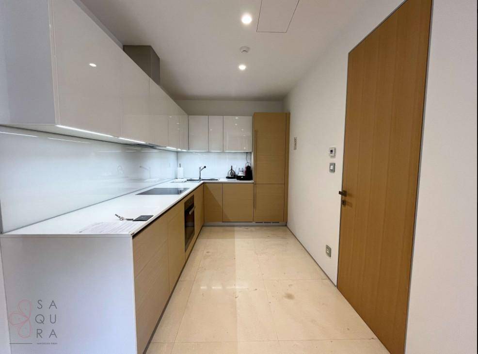 Schlanke moderne Küche mit hellen Holz- und weißen Hochglanzfronten, integrierten Geräten und Fliesenboden.