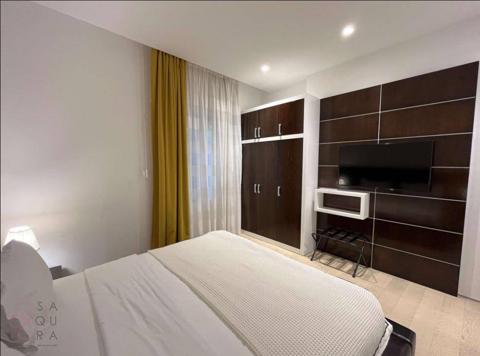 Modernes Schlafzimmer mit großem Bett, Einbauschrank und Fernseher an einer dunklen Holzwand.